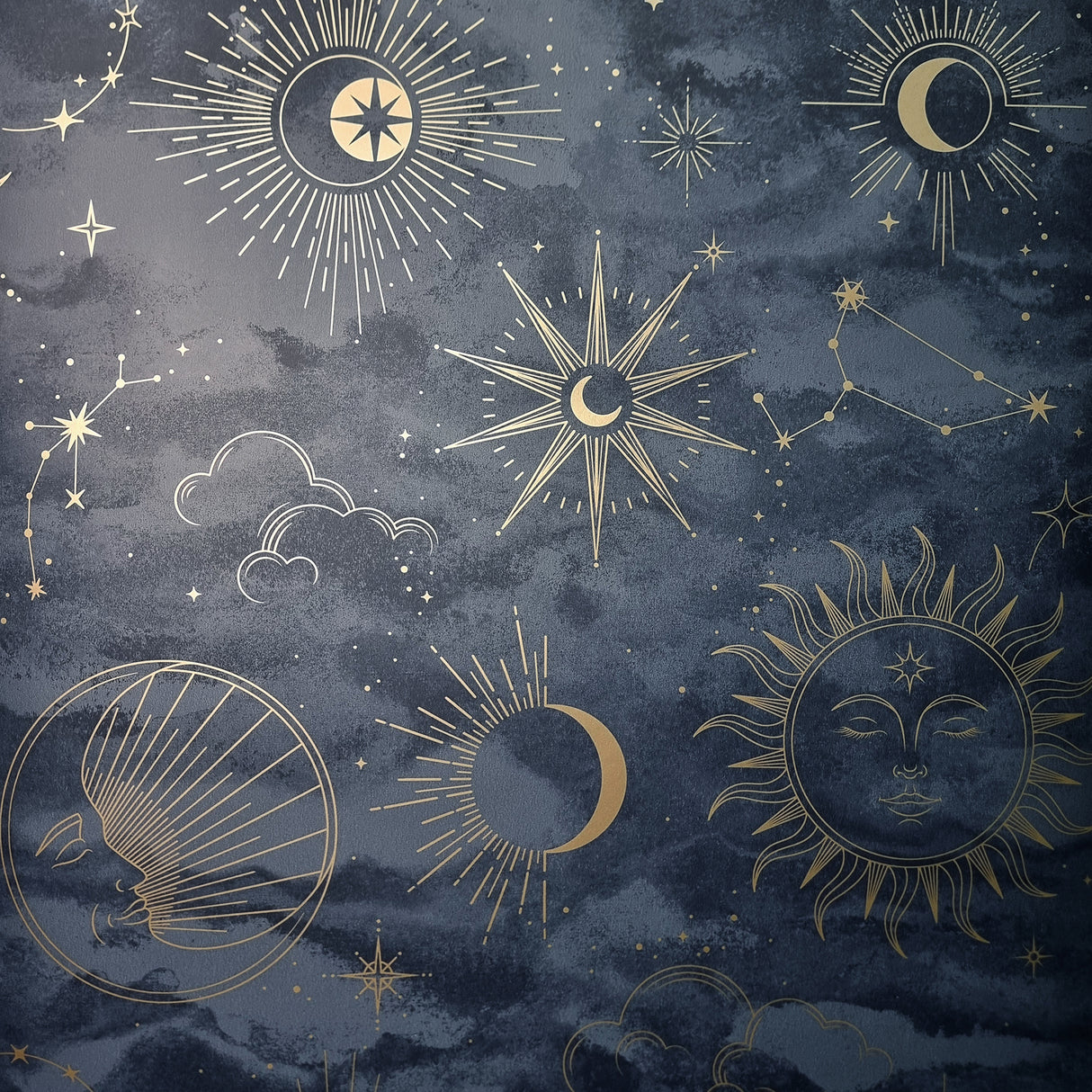 Kalel Navy celestial wallpaper with gold suns, moons, stars, and constellations on a mottled blue sky background.