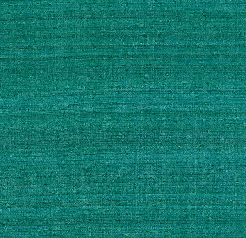 Shaded Silk Peacock wallcovering by Schumacher in a teal blue-green silk texture, shown in a styled interior with a velvet chair.