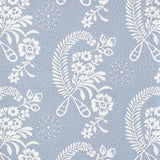 Millicent Delft wallpaper by Schumacher, featuring a delicate white floral and botanical pattern on a blue background, shown in a styled bathroom interior.