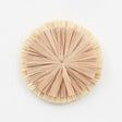 Large natural raffia flower wall decor from Schumacher, shown in close-up and styled on a wall above a fireplace and sofa.