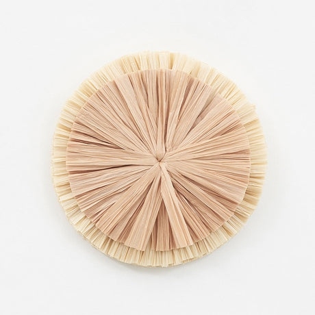 Large natural raffia flower wall decor from Schumacher, shown in close-up and styled on a wall above a fireplace and sofa.