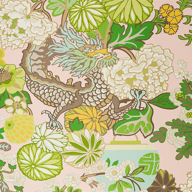Chiang Mai Dragon Blush wallpaper by Schumacher featuring a vibrant chinoiserie dragon and floral motif in green, yellow, and white on a blush pink background.
